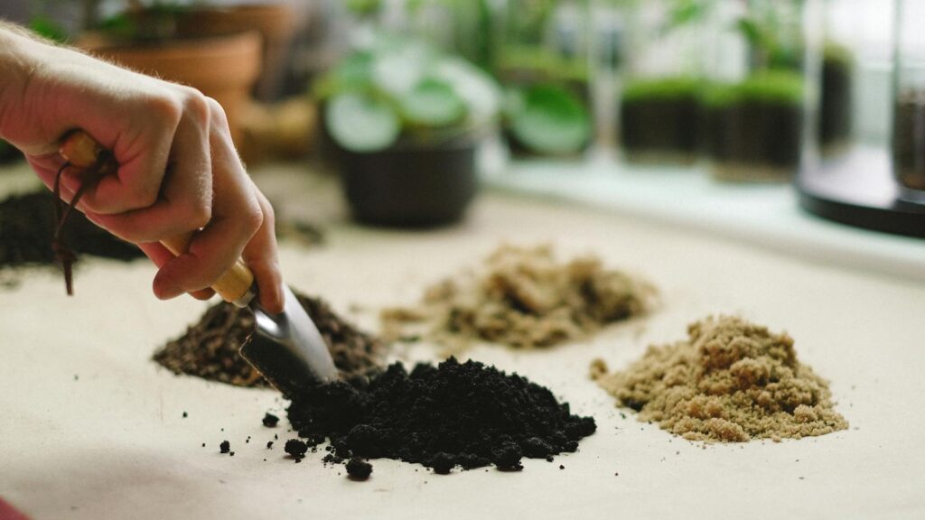 Hand scooping dark soil with a trowel beside other soil types.