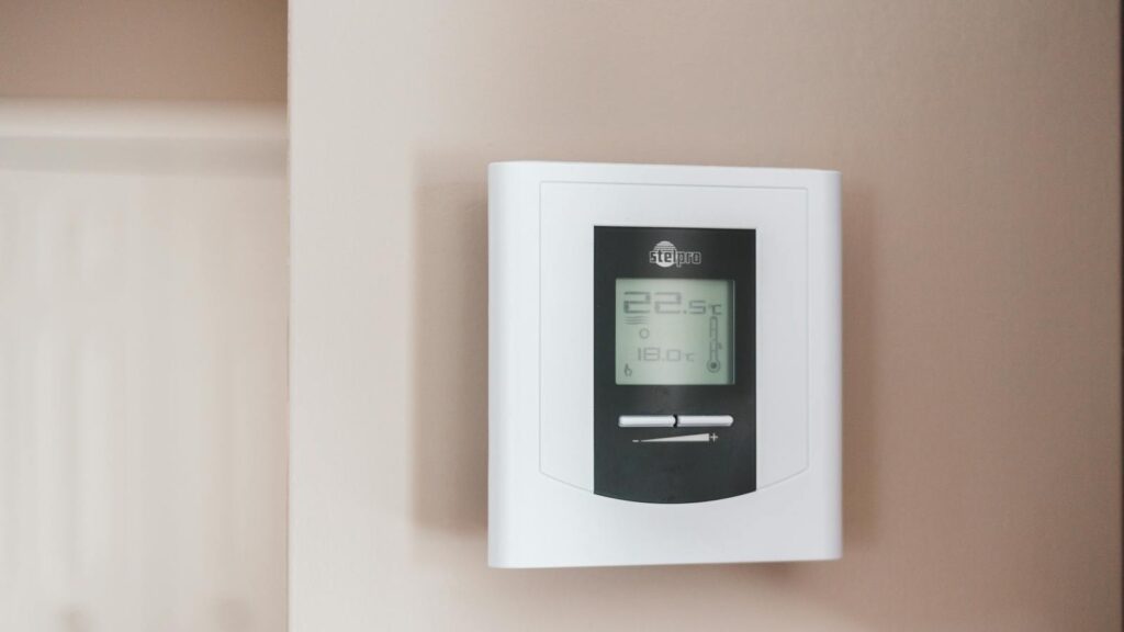 Modern digital thermostat mounted on a beige interior wall.
