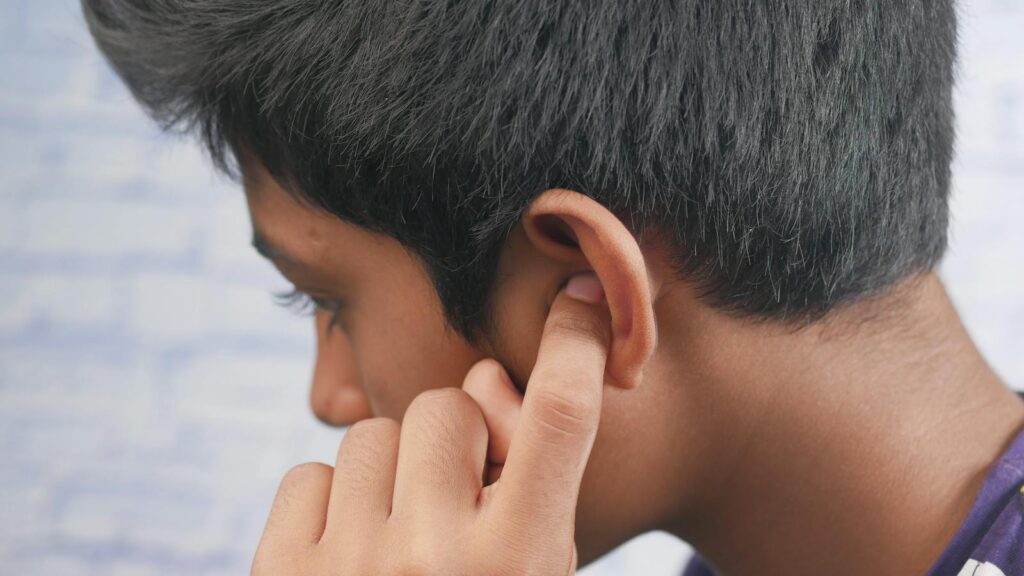 Close-up of a teenager's profile with hand covering ear, reflecting introspection or concentration.