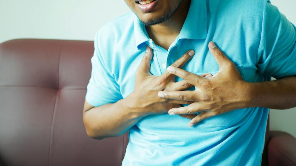 A close-up image of a man clutching his chest, indicating heart pain or discomfort.