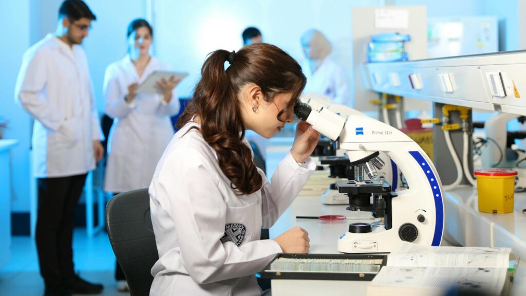 Young female scientist examining samples under a microscope in a modern laboratory setting.