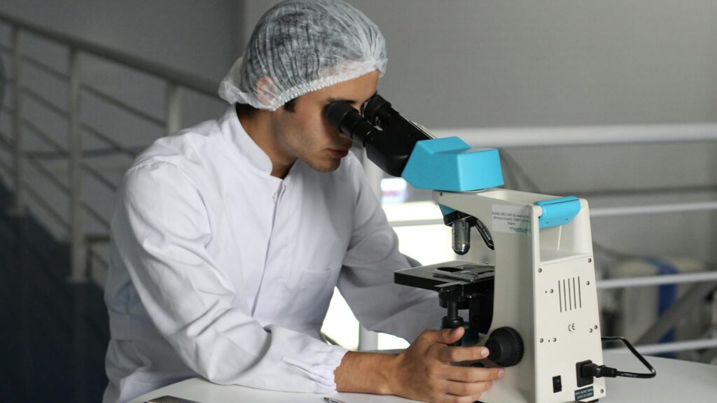 Scientist in a lab coat using a microscope to conduct research, focusing on healthcare improvements.