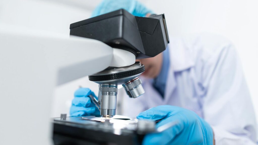 Close-up of a scientist examining samples under a microscope in a lab setting.