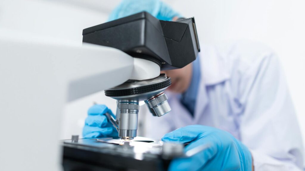 Close-up of a scientist examining samples under a microscope in a lab setting.