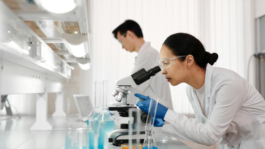 Two scientists in a lab examining samples with a microscope. Focus on scientific research and discovery.