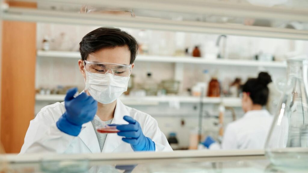 Researcher in a lab coat working on a scientific experiment with a petri dish and protective gear.