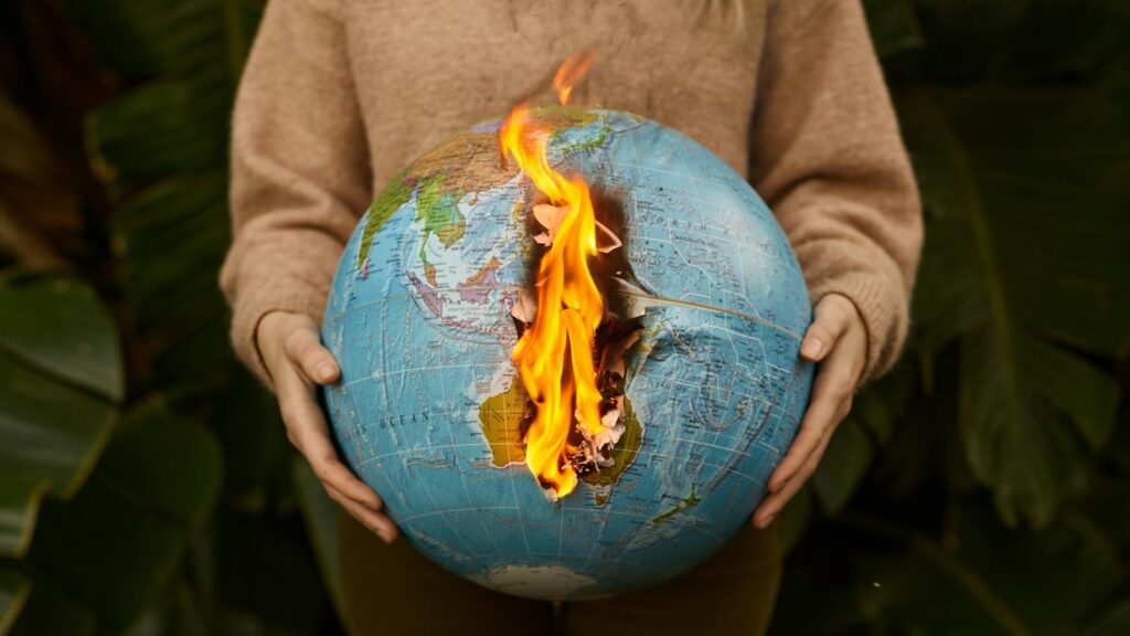 A symbolic portrayal of climate change with a burning globe held in hands, set against a nature background.