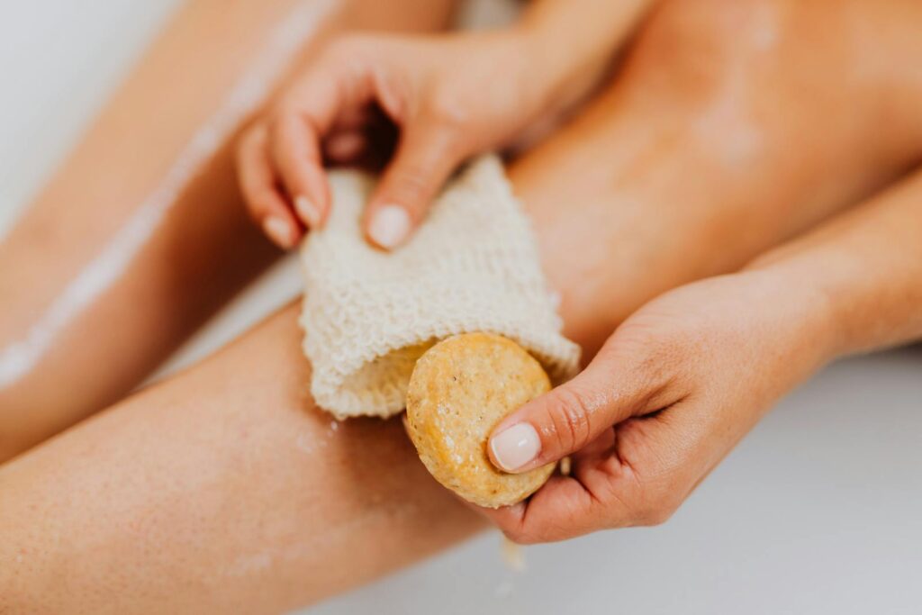 Detailed view of hands scrubbing a leg with soap and exfoliating mitt.