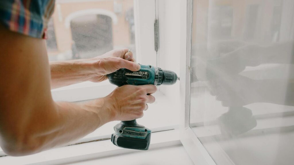 A person using an electric drill to repair or install a window indoors.