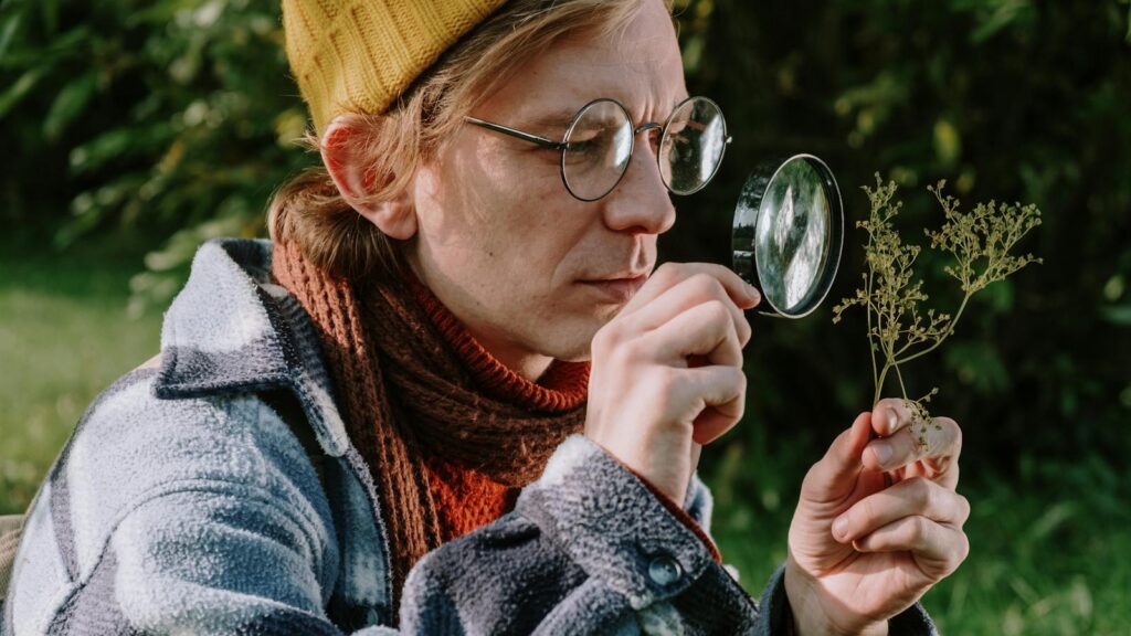 A botanist examines a plant with a magnifying glass in an autumn garden setting.