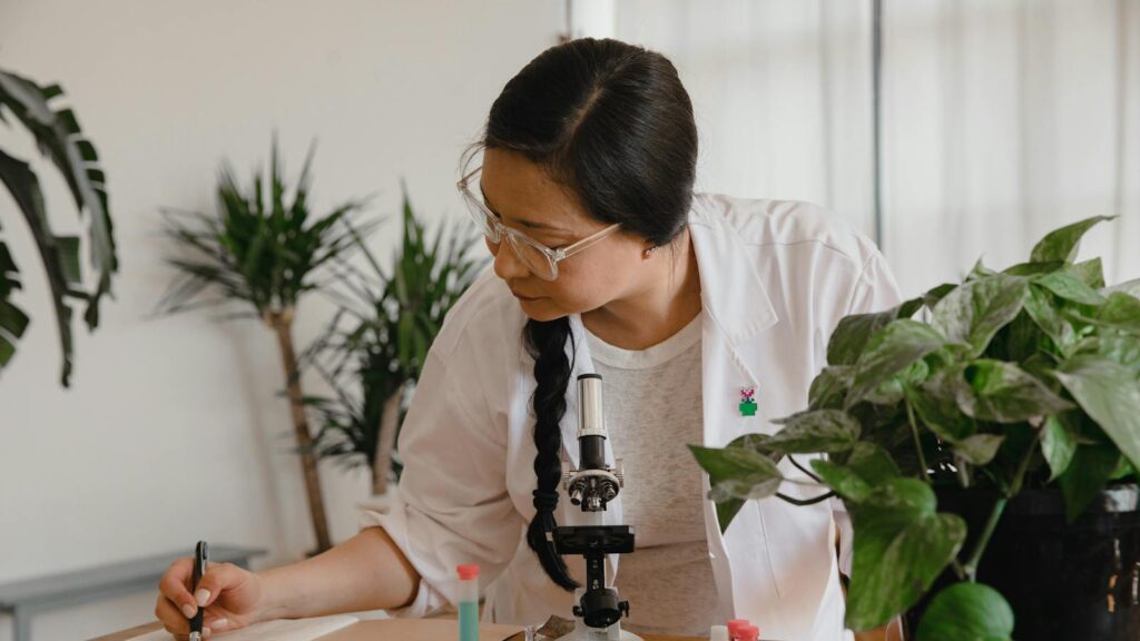 Female scientist conducting research and taking notes with microscope and plants.