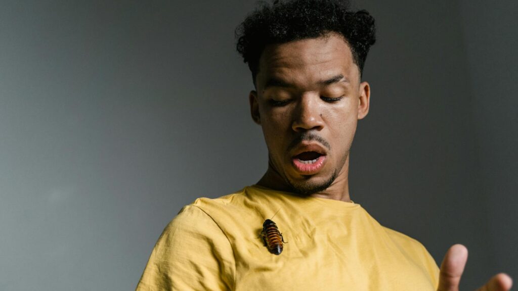 A man looks startled as a cockroach sits on his yellow shirt.
