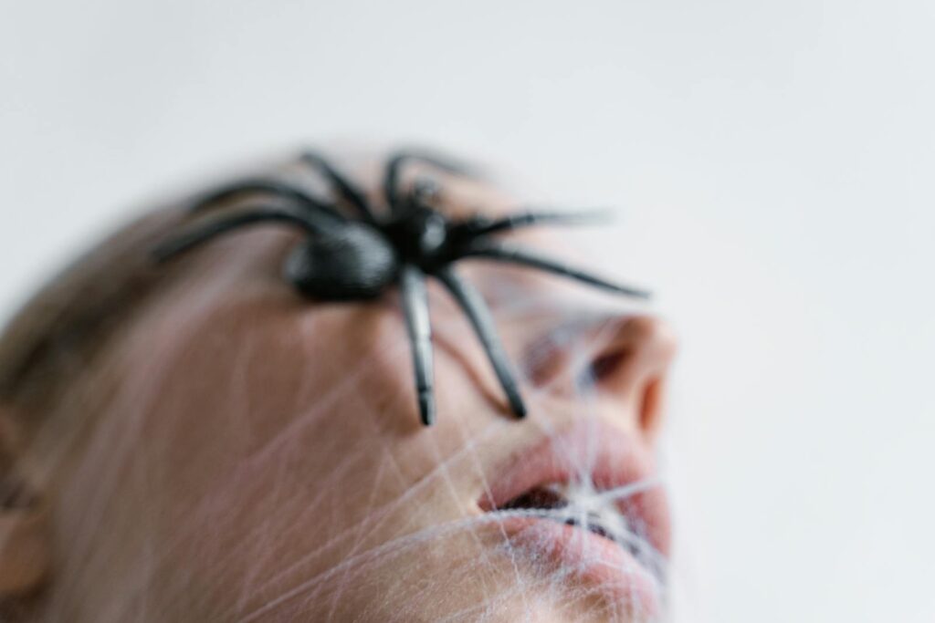 A dramatic close-up of a spider on a face covered in webbing, evoking fear and entrapment.