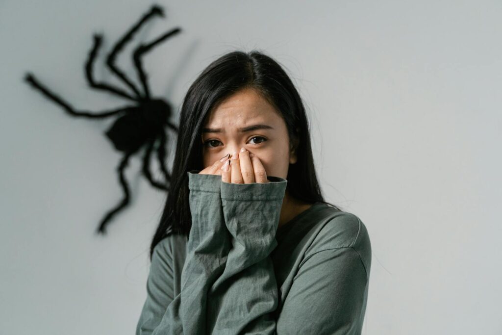 An anxious woman indoors with a large wall spider, depicting arachnophobia.