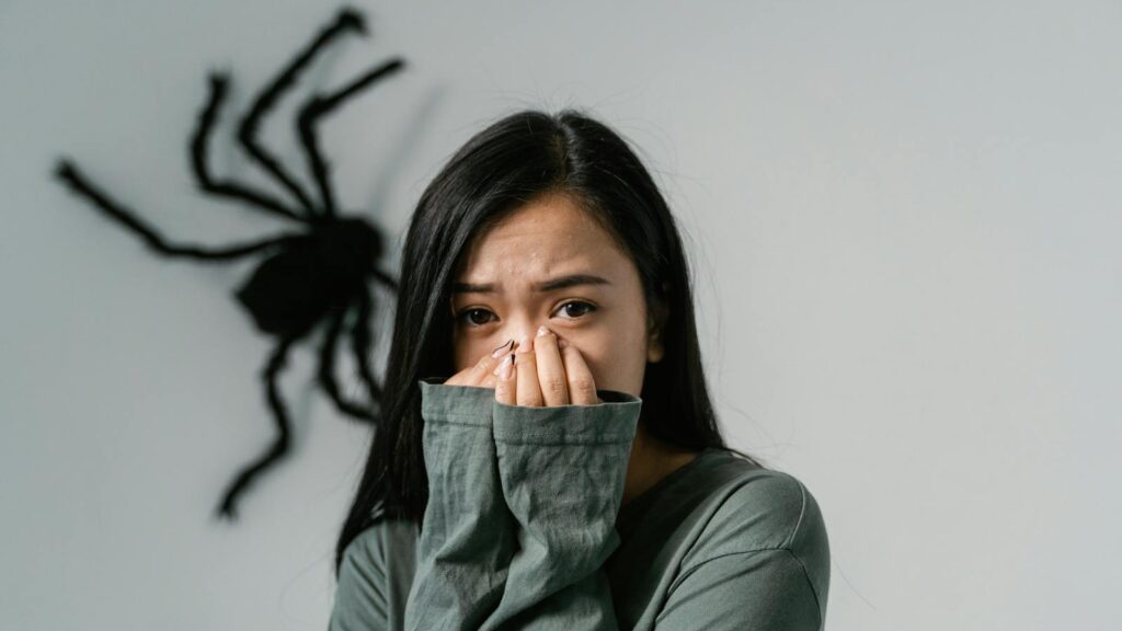 An anxious woman indoors with a large wall spider, depicting arachnophobia.