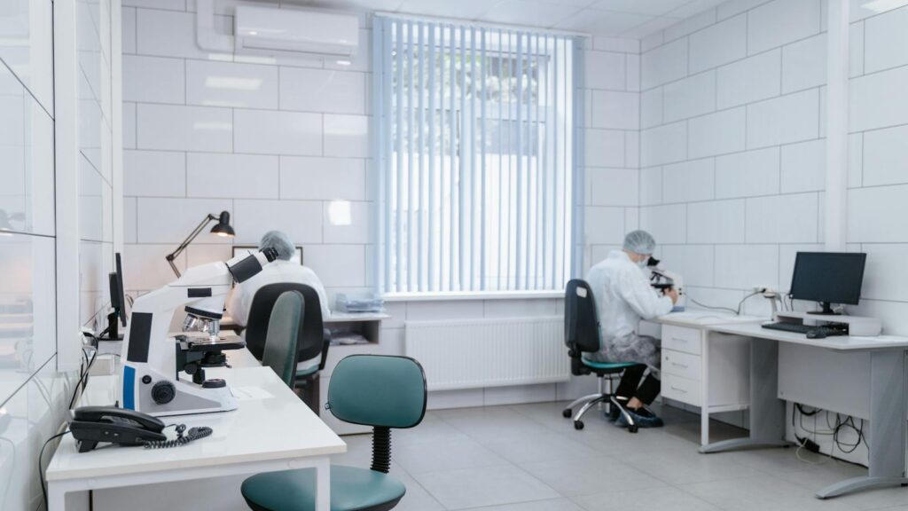 Clean, modern laboratory interior with microscopes and researchers in protective gear conducting analysis.