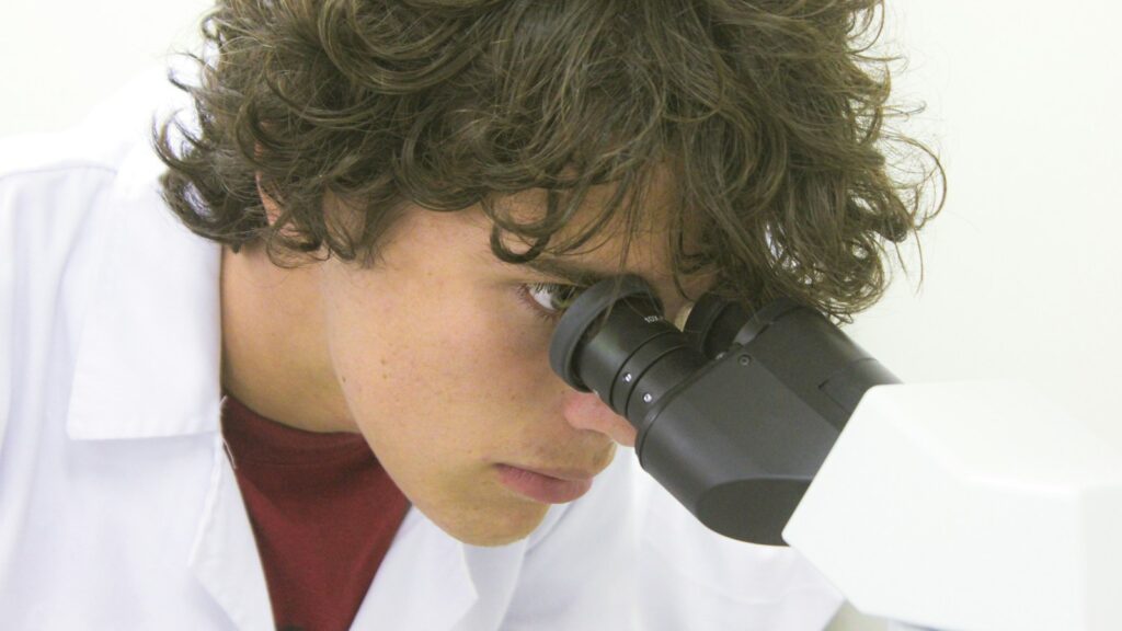 A young scientist examines through a microscope.