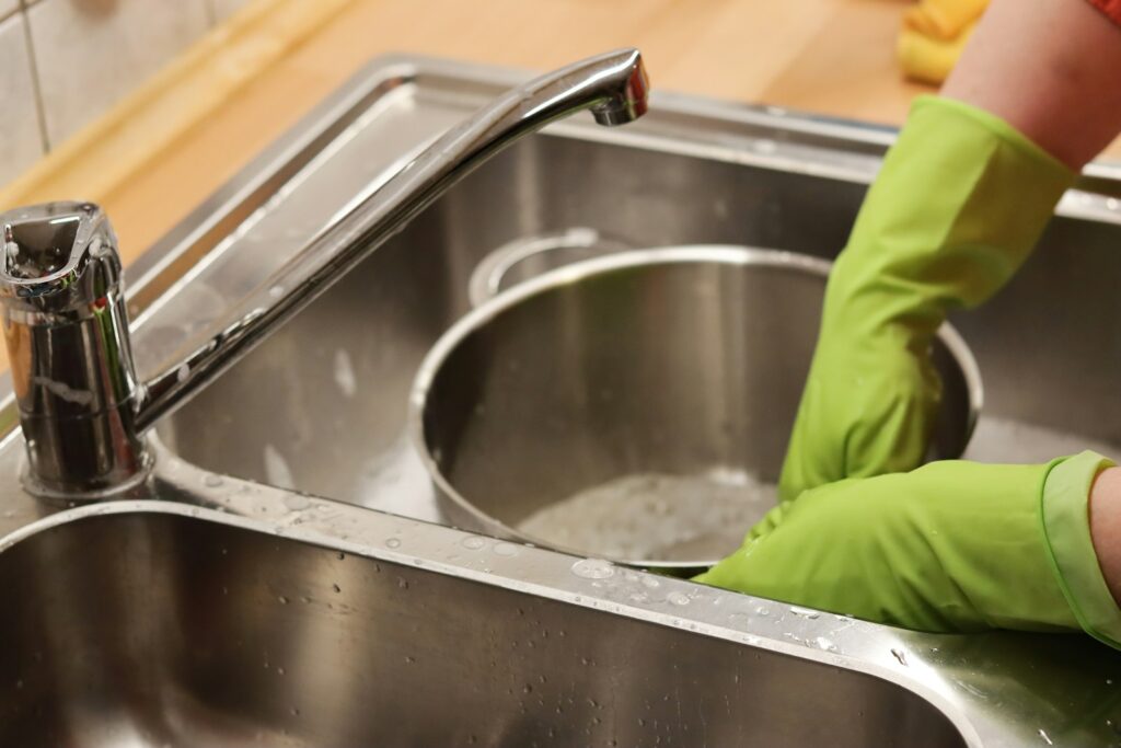 Person in green gloves washing stainless steel bowl in a sink