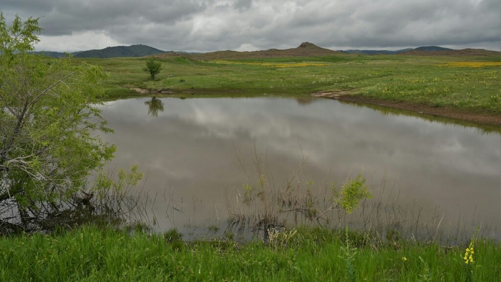 a small lake surrounded by green grass and hills